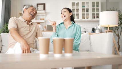 Happy elderly couple enjoying a ball toss game together at home, practicing coordination and cognitive skills for healthy aging. Grandfather and grandmother throwing ping pong in the bowl. Myrmidon.