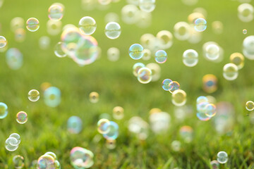 Many beautiful soap bubbles floating above green grass