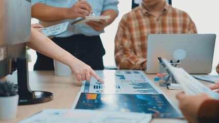 A group of professionals engages in a collaborative meeting, analyzing data charts and discussing insights in a contemporary workspace filled with technology and documents. SACTR
