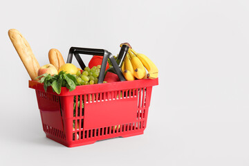Red shopping basket full of different fresh products and baguette on white background