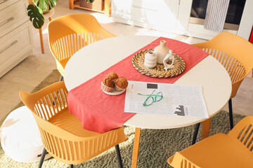 Eyeglasses with newspaper and muffins on dining table in kitchen
