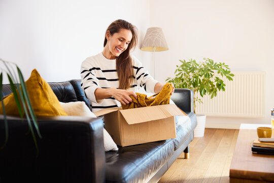 Smiling woman unpacking online clothes order sitting on sofa at home