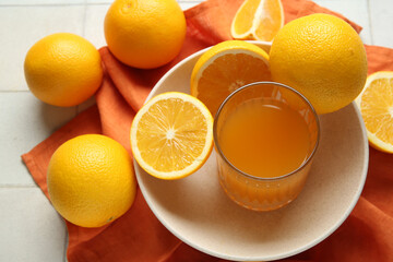 Glass of fresh orange juice and plate with fruits on white tile background