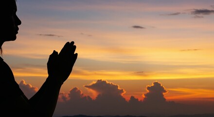 Silhouette of a person praying at sunset with vibrant clouds in the background
