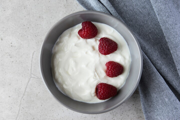 Gray bowl and natural yogurt with berries on the stone marble table.