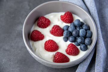 Gray bowl and natural yogurt with berries on the stone marble table.