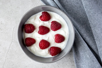 Gray bowl and natural yogurt with berries on the stone marble table.