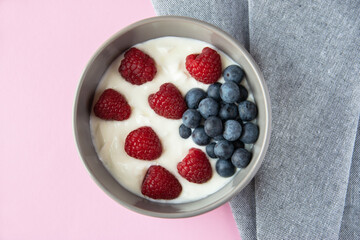 Gray bowl and natural yogurt with berries on the pink background.