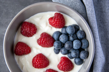 Gray bowl and natural yogurt with berries on the stone marble table.