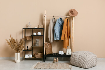 Rack with autumn clothes and pouf in stylish interior of hallway