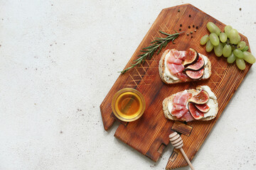 Wooden board of delicious fig bruschetta with prosciutto and ricotta cheese on white background