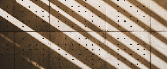 Beige concrete wall texture with diagonal sunbeams and regularly spaced holes, creating a geometric pattern ideal for architectural or design backgrounds