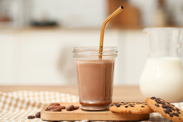 Glass of sweet chocolate milk with cocoa beans and tasty cookies on wooden table in kitchen