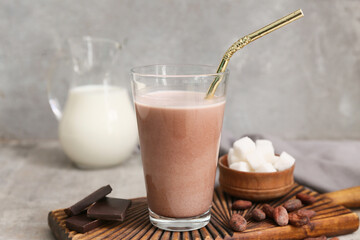 Glass of sweet chocolate milk with cocoa beans and cubes of sugar on grey background