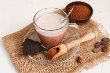 Glass cup of sweet chocolate milk with beans and bowl of cocoa powder on white background