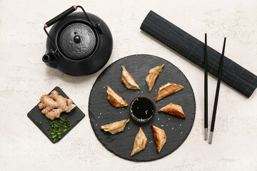 Black board of fried Japanese gyoza with sesame seeds and bowl of soy sauce on white background