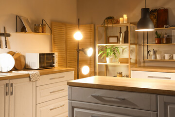 Interior of kitchen with counters, shelves and glowing lamps in evening