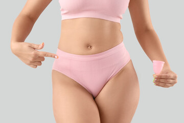 Young woman in underwear with menstrual cup on light background, closeup