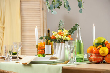 Table setting with citrus fruits, bottles of drink and flowers in living room. Closeup