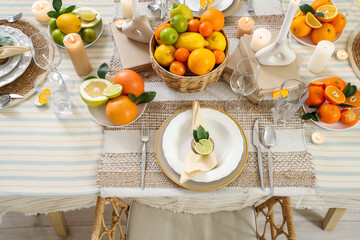 Festive table setting in dining room decorated with citrus fruits. Closeup