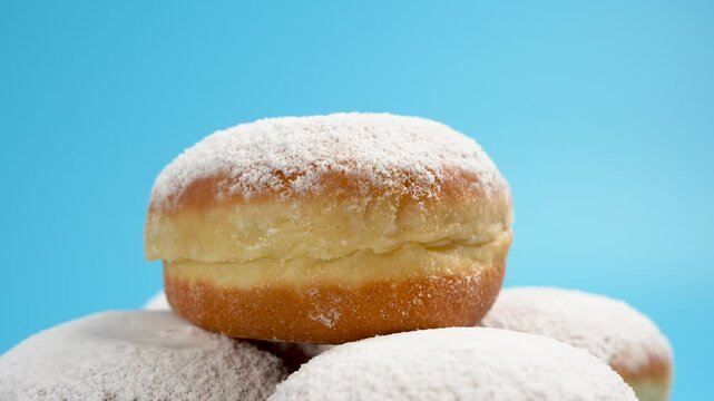 A donut with powdered sugar is placed on top of a stack of other donuts. The donut is covered in powdered sugar and is spinning on a blue background.