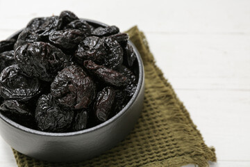 Bowl with dried prunes on white wooden background