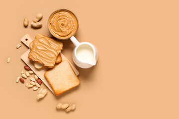 Bowl with tasty peanut butter, jug of milk, toasts and nuts on beige background
