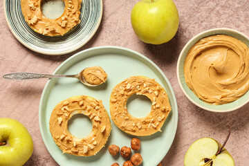 Plates with apple rounds, bowl of nut butter and hazelnuts on pink grunge background