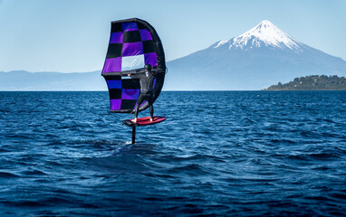 A young man in a wetsuit performs wing foil on a calm lake in southern Chile, surrounded by breathtaking nature. The sport combines wind, water, and adrenaline for an adventurous experience.