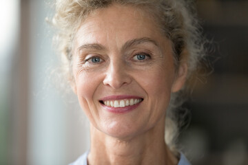 Ageless beauty. Close up portrait beautiful face happy older woman with curly blond hair light...