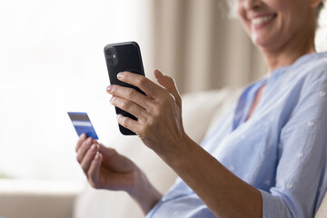 Close up cropped shot smiling aged female holding smartphone credit bank card in hands. Safe online...