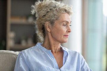 Moment of reflection. Head shot portrait calm pensive beautiful older age woman relaxing in living...