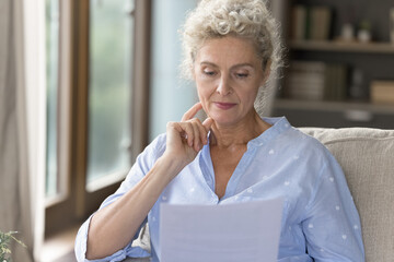 Reviewing papers. Thoughtful old lady sit on sofa study documents with pension information ponder...