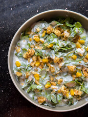 Creamy purslane salad with greens, corn, and walnuts in beige bowl. Round bowl of healthy purslane salad with dressing. Fresh ingredients, healthy eating and nutrition concept