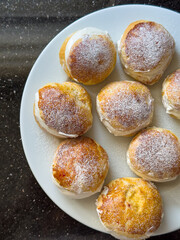 Homemade Berliner donuts pastries with powdered sugar and cream filling. Delicious Berliner or Krapfen buns dessert served on a white plate. Jam doughnut, German pastry and sweet concept