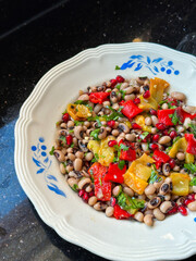 Colorful black bean salad with roasted peppers, herbs, and pomegranate on decorative plate. Fresh mediterranean black eyed pea salad. Healthy eating, nutrition and wholesome meals concept