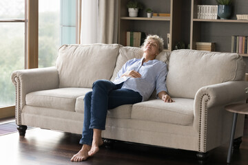 Serenity in solitude. Tranquil older age lady retiree recline on cozy sofa with closed eyes enjoy...