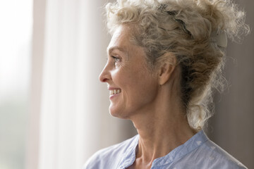 Confidence and grace. Close up profile portrait elegant beautiful elderly woman with stylish curly blond hairdo posing indoors looking forward with optimism showing bright perfect smile. Copy space © fizkes
