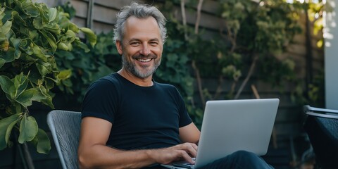 A man is sitting on a chair with a laptop in front of him. He is smiling and he is enjoying himself