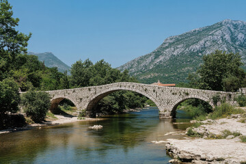 Fototapeta premium Old stone bridge arching over calm river in montenegro countryside