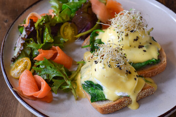Closeup breakfast plate with eggs benedict, smoked salmon and fresh greens salad