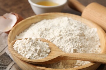 Flour in bowl, spoon and rolling pin on table, closeup