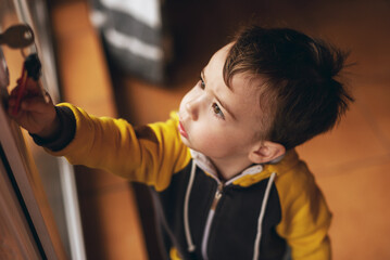 A small child carefully examines the keys stuck in the front door. The child is alone at home