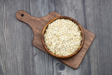 Oat flakes uncooked in a brown bowl on wooden table. Healthy food for breakfast
