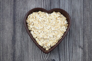 Oatmeal flakes and oats on a heart shaped plate on black background. Healthy breakfast. Organic and vegetarian food.