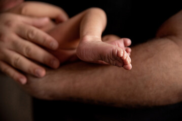 The newborn's little foot rests on the father's hand