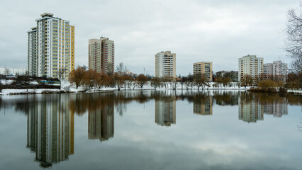 A modern residential area by a water body in the city, showcasing new home construction and the demolition of older structures. The urban landscape reflects the transition of winter into spring.