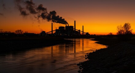 Fototapeta premium Industrial Sunset Reflection - Silhouette of an industrial power plant at sunset, reflected in calm water. Pollution is visible