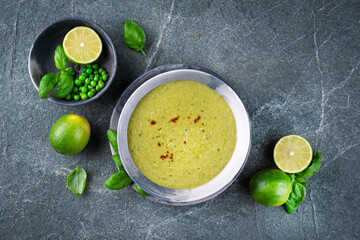 Fresh spicy creamy green pea soup pureed blend with lime and basil served as top view in a design bowl