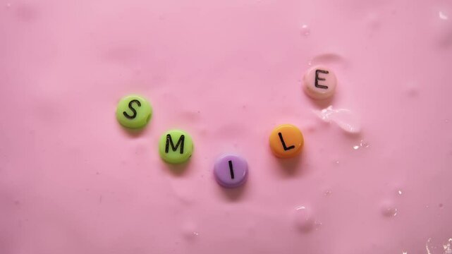 Teenager's hands were creating a smile out of small, round, multicolored letters on top of a pink, stringy slime.
